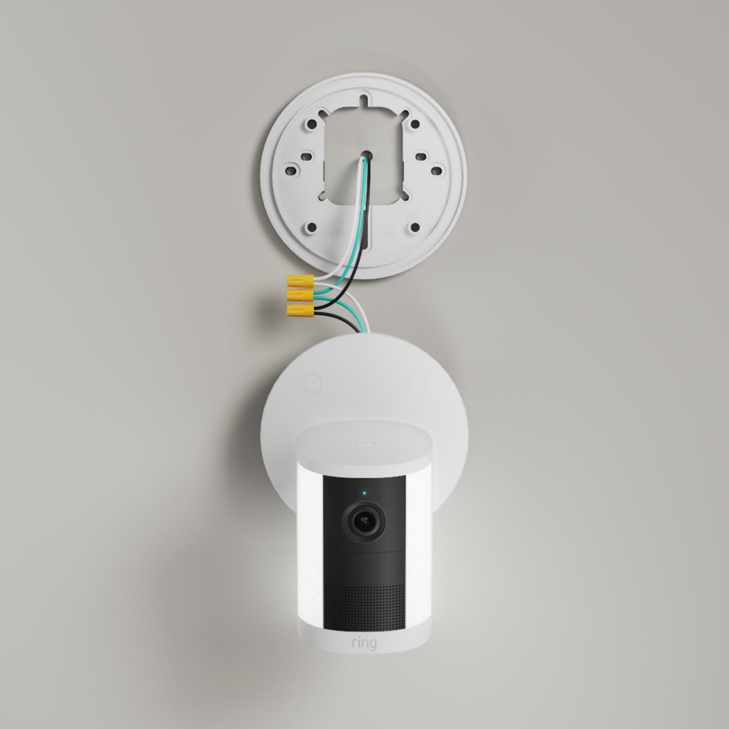 Spotlight Cam (Newest Model) - Wired:White Ring Spotlight Cam (2nd Gen) mounted to a wall with mounted hardware connected on a gray wall.