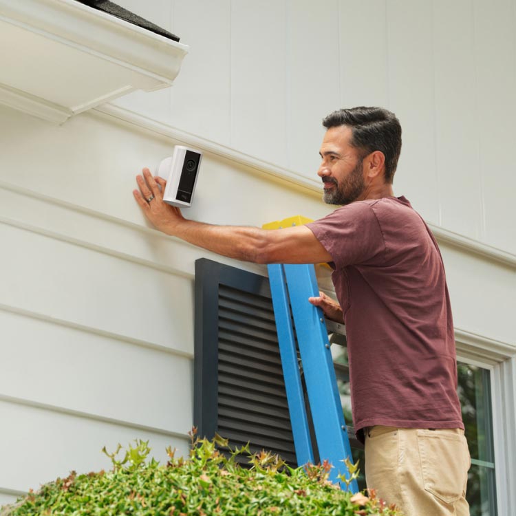 Man on a ladder mounting a white Spotlight Cam Pro (2nd Gen) onto the side of his home.