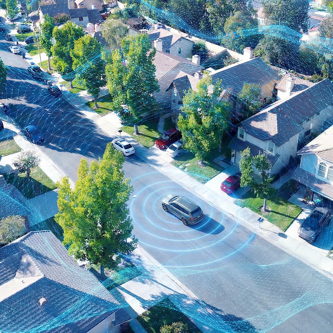 Aerial view of a suburban street with a black car surrounded by blue digital waves, illustrating connected vehicle tech among homes and trees