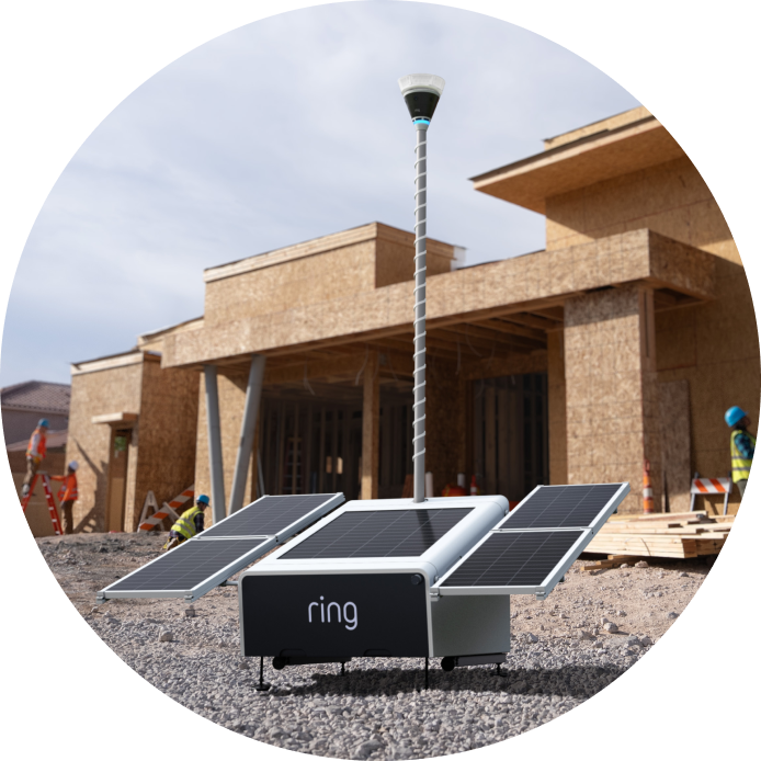 Portable Ring device with four solar panels and a tall mast set up at a wooden house construction site, workers in hard hats nearby.