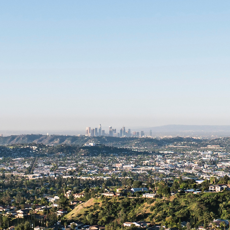 A panoramic view of a city skyline with rolling hills in the foreground under a clear blue sky.