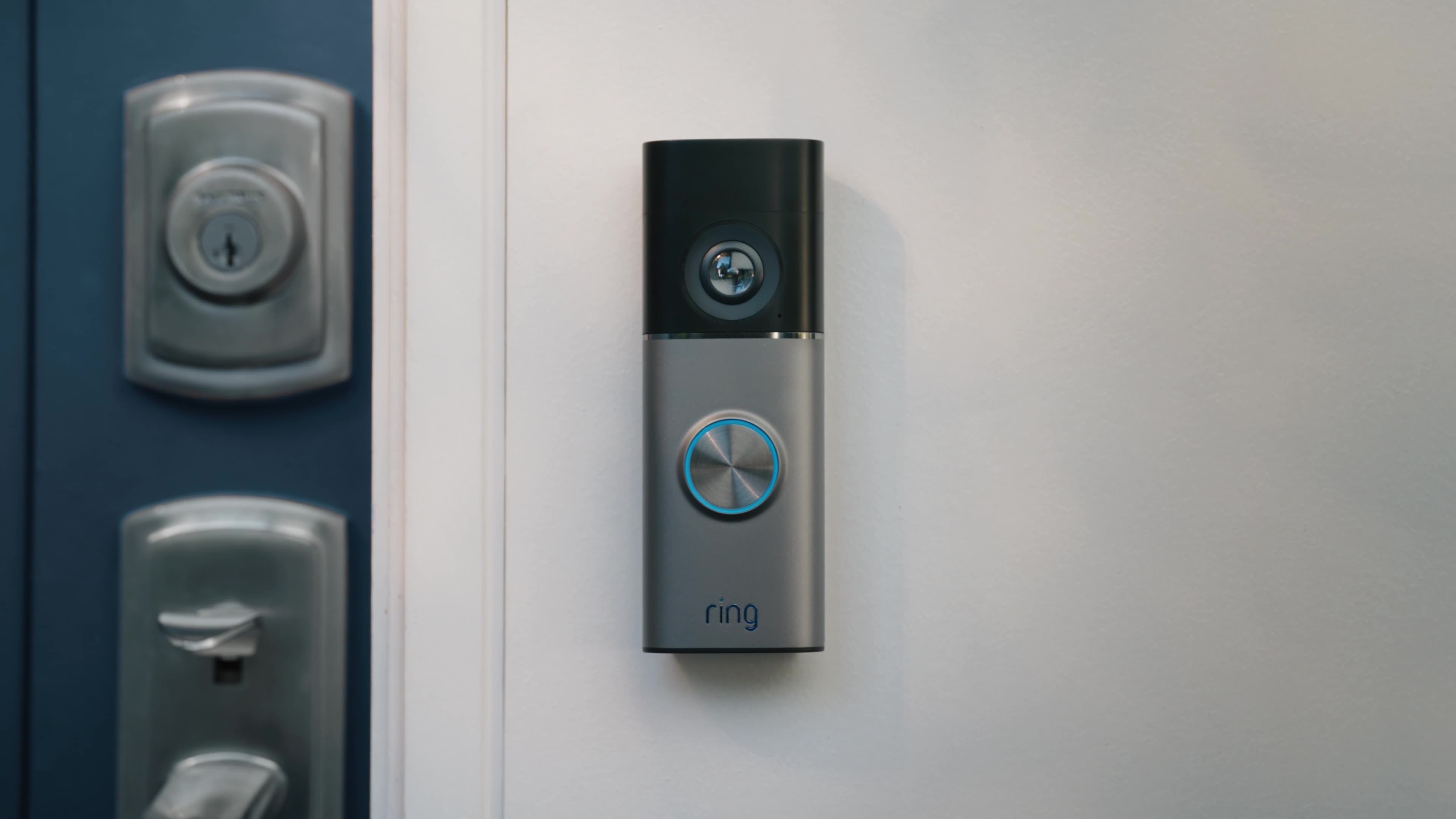 Wired Video Doorbell Pro (3rd Gen) mounted next to a blue door with lock on a door frame. Play button overlay is in the center of the image.