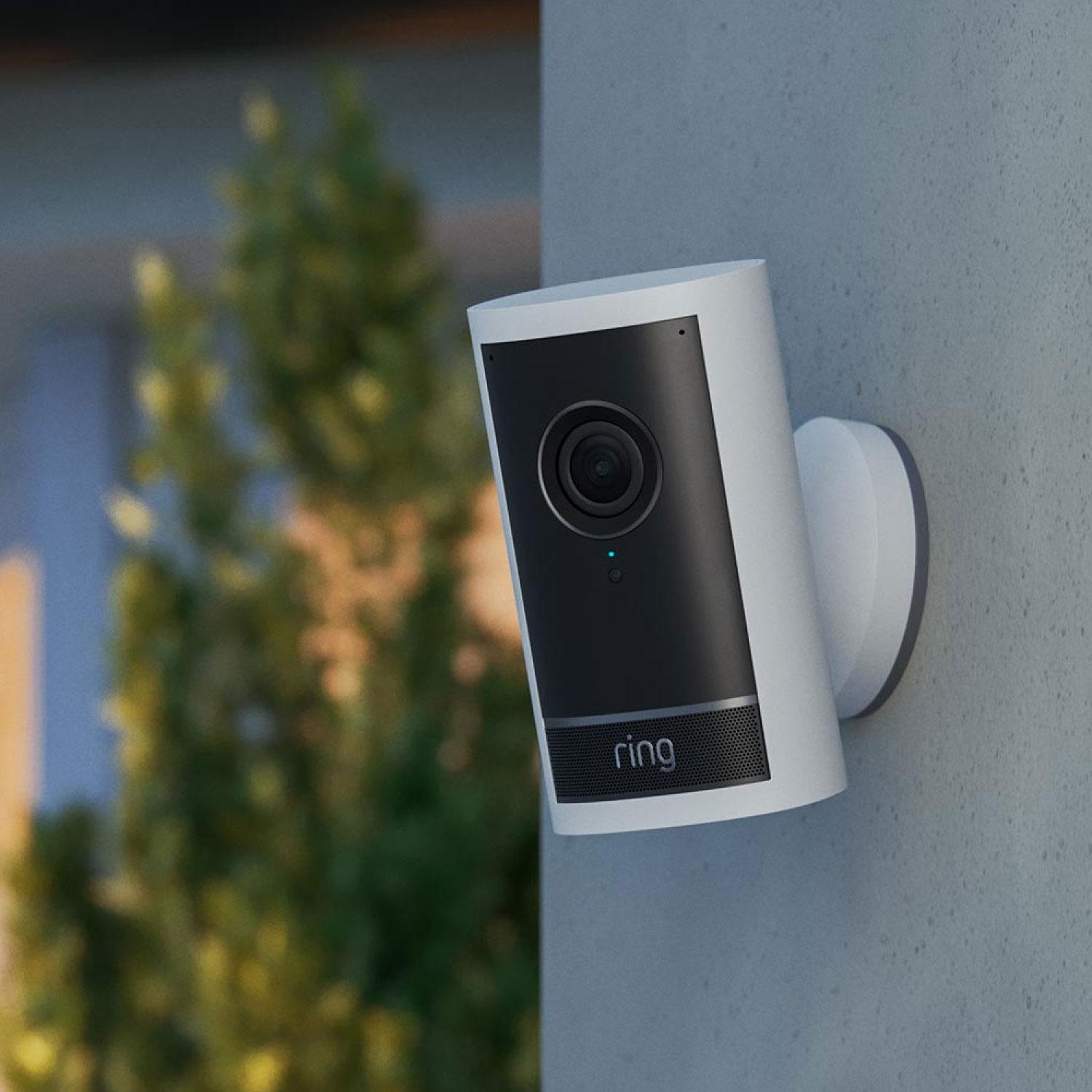 PoE+ Converter Mount - White Outdoor Cam Pro mounted on a stone exterior wall using a white PoE plus Converter Mount with green foliage in the background.