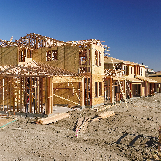 New homes under construction with wooden frames and plywood sheathing against a clear blue sky.