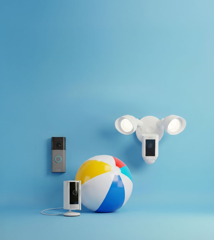 Smart home devices against a blue backdrop: a video doorbell, a plug-in indoor camera, and a white floodlight camera beside a beach ball.