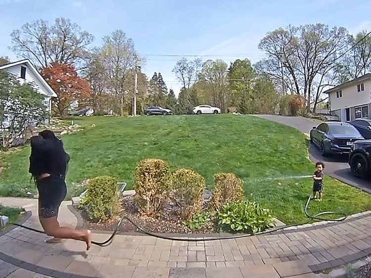 Child holding water hose while spraying their aunt.