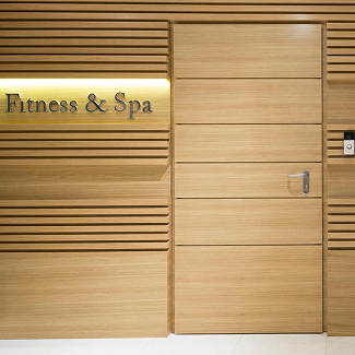 Wood-paneled wall with a door labeled Fitness & Spa, lit sign on the left and a small doorbell or intercom panel on the right.