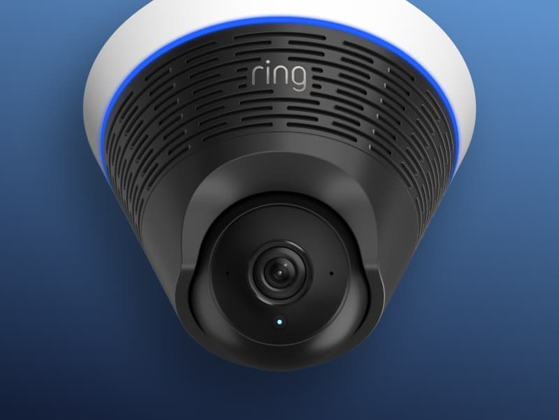 Close-up of a ceiling-mounted Ring security camera against a blue background.