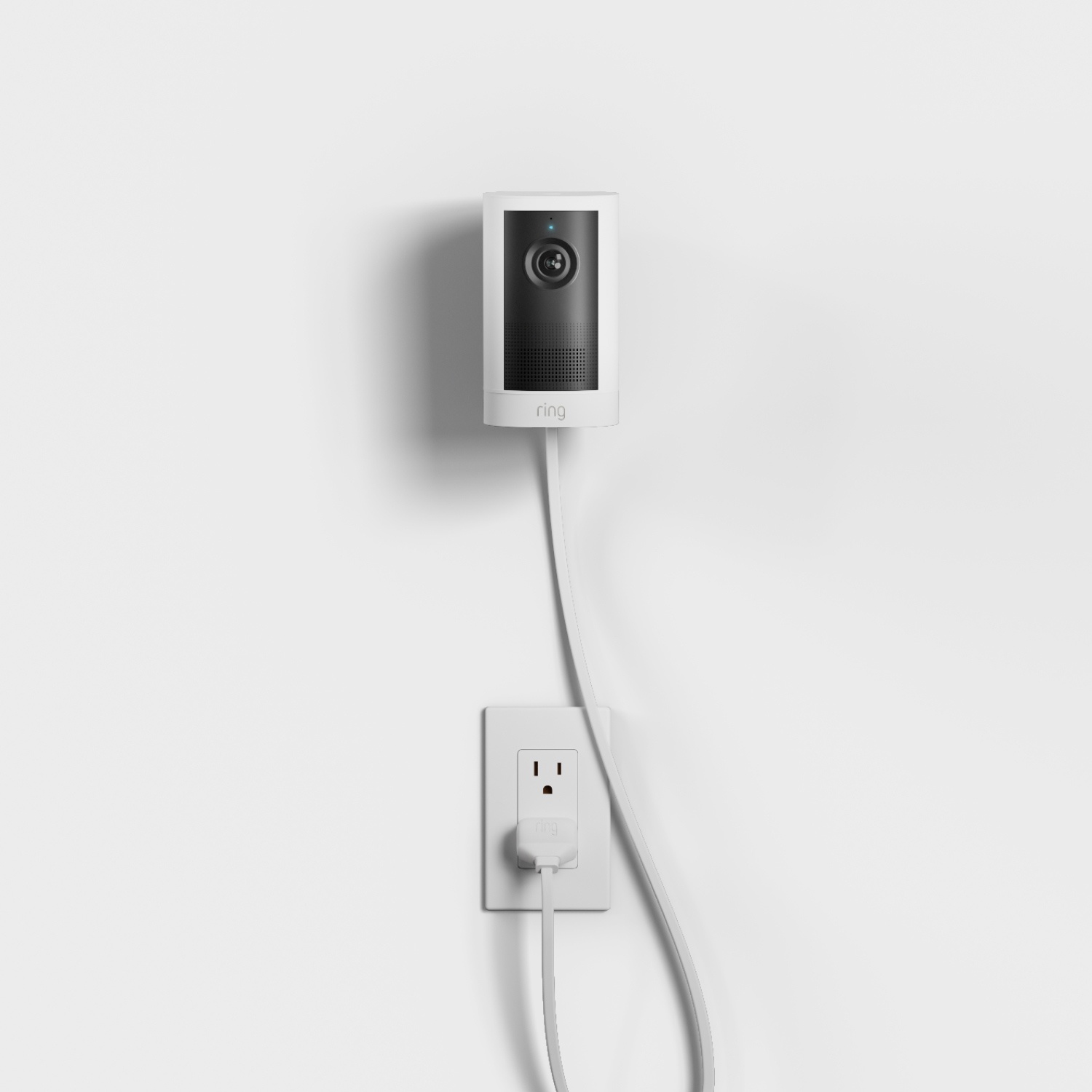 Outdoor Cam 4K Plus  - Plug-In:White indoor Ring camera mounted on a wall, plugged into a nearby outlet with a long white power cord.