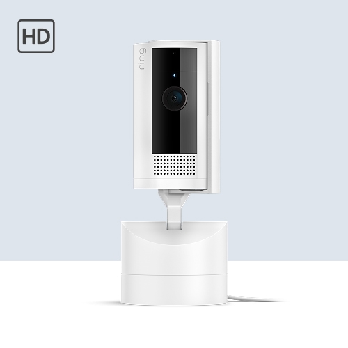 White Ring indoor camera on a stand with black lens panel and speaker grille, shown against a light blue background with an HD icon.