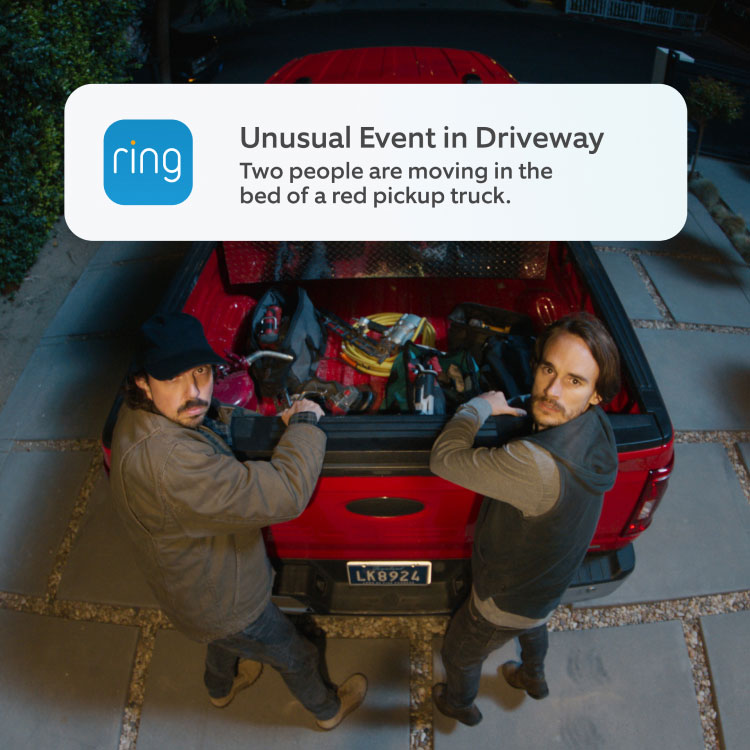 Nighttime driveway scene: two people at a red pickup’s open bed, handling tools under outdoor lights. A popup with the Ring logo on the left is headlined 