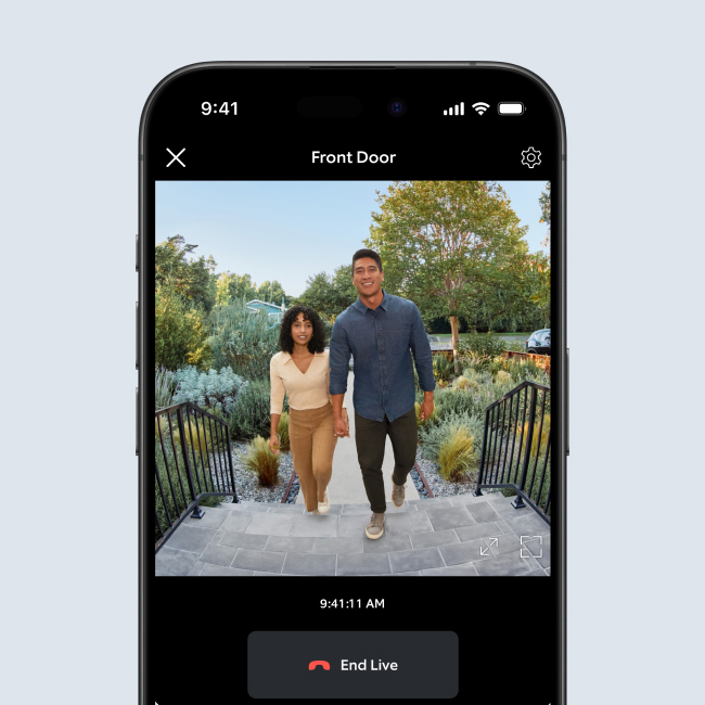 Smartphone displaying live Ring Doorbell feed of a smiling couple holding hands and walking up front steps.