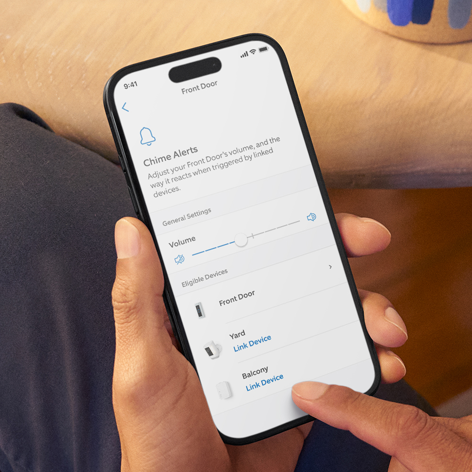 Chime Plus - Hand holding a smartphone showing a home app screen for Front Door chime alerts, with a volume slider and options to link Yard and Balcony devices.