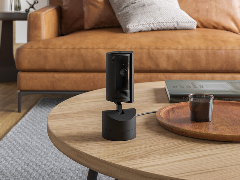 Black Pan-Tilt Indoor Cam sitting on a wooden coffee table next to a brown sofa.