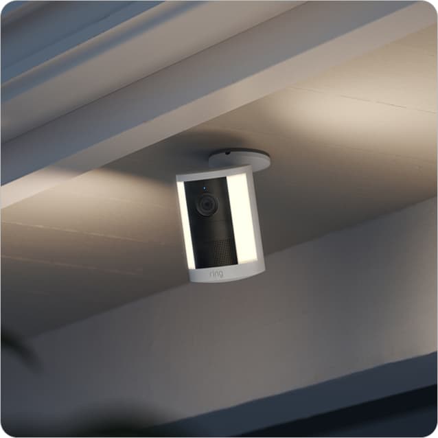 Spotlight Cam (2nd Gen) mounted under a porch eave at dusk, casting soft light on the entryway.