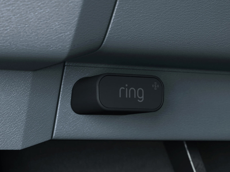 Close-up of a small black Ring-branded device mounted under a gray car dashboard.