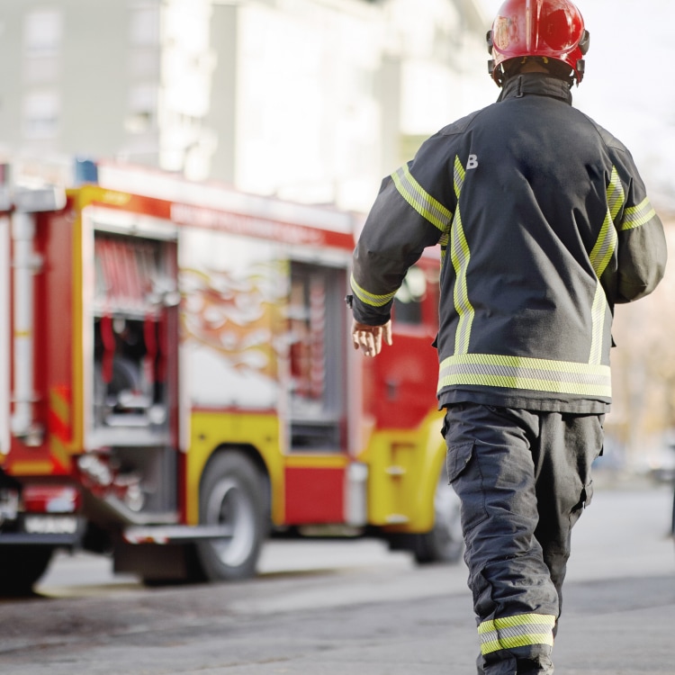 A firefighter in protective gear and a red helmet walks toward a red and yellow fire truck.