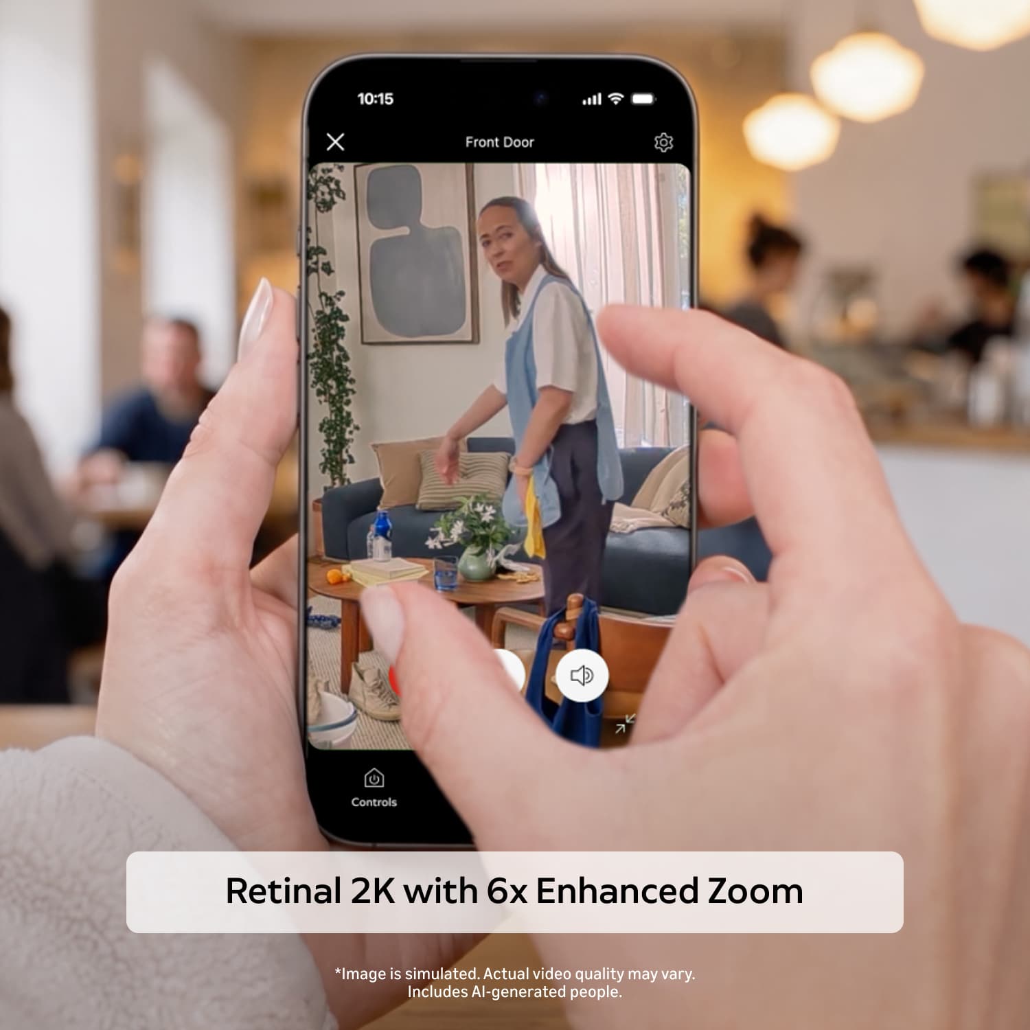 Pan-Tilt Indoor Cam 2K - Hands holding a smartphone showing a home entry camera feed, zoomed on a living room where a person stands near a sofa and table.