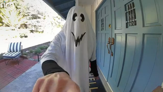 A person in a ghost costume is scared by an adult and two kids in skeleton costumes.