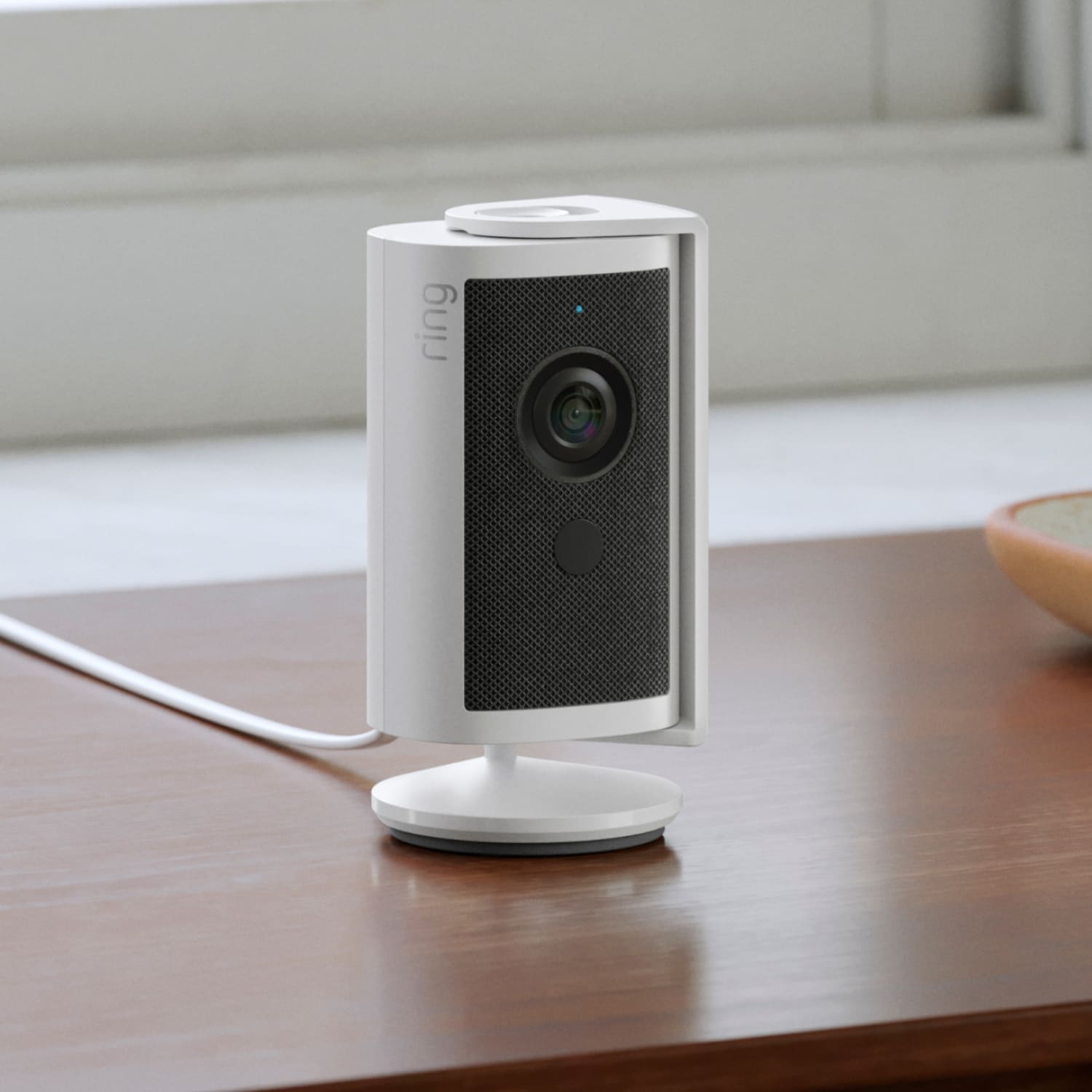 Indoor Cam 4K - Plug-In:Indoor Cam 4K sitting on a wooden table near a window, powered by a white cable.