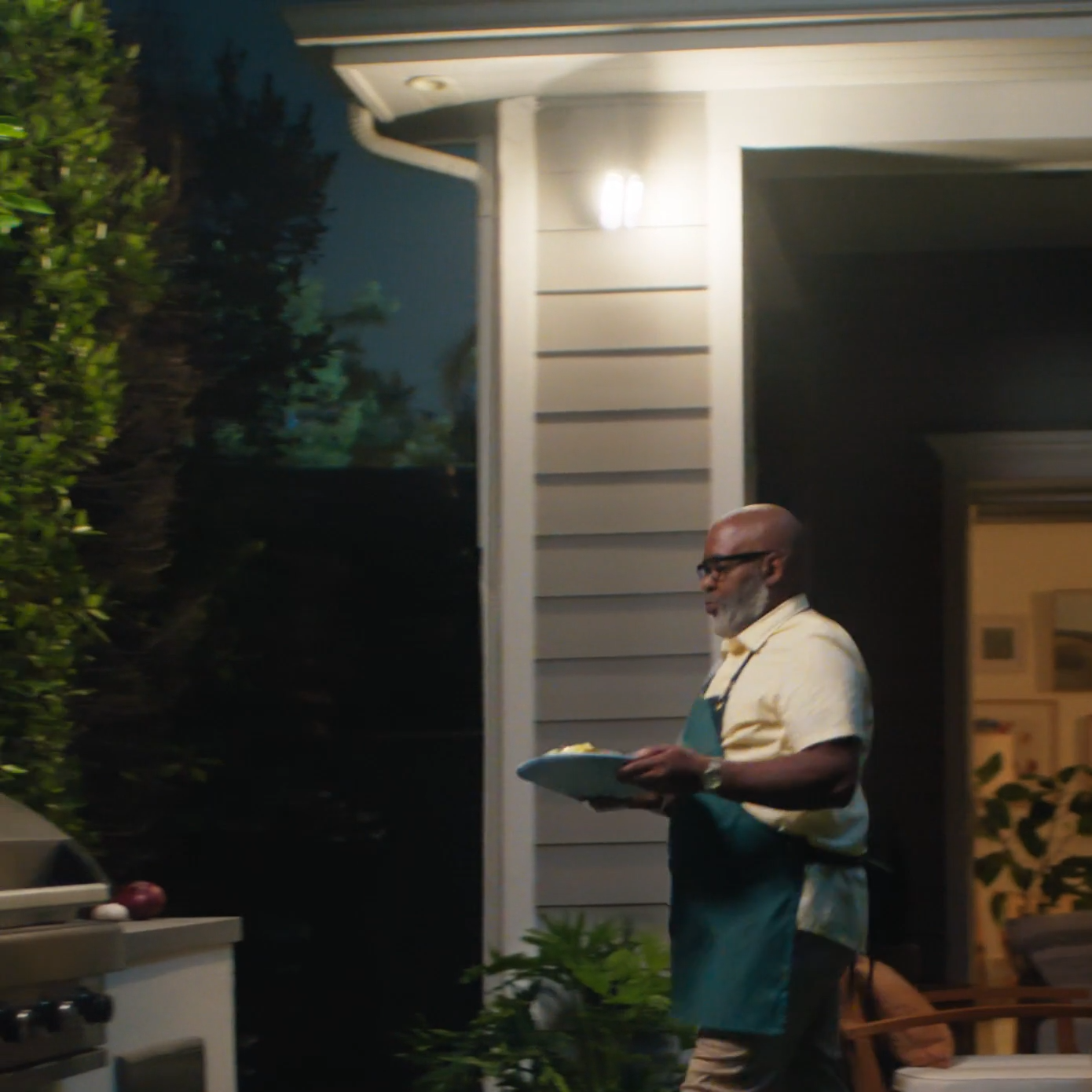 Man walking through backyard to bbq with Security camera lights on 