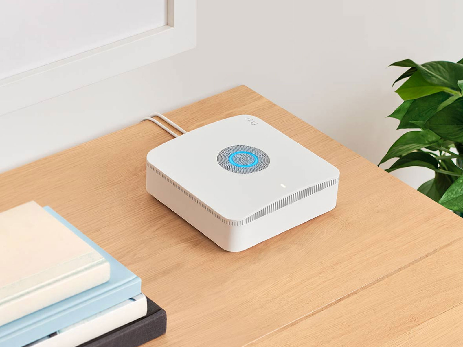 A white square Alarm Base station sits on a wooden shelf in a living room.