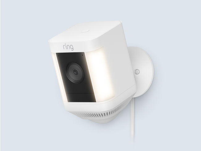 White Ring Spotlight Cam Plus Plug-In, with built-in motion-activated LED lights, mounted on an outdoor wall.