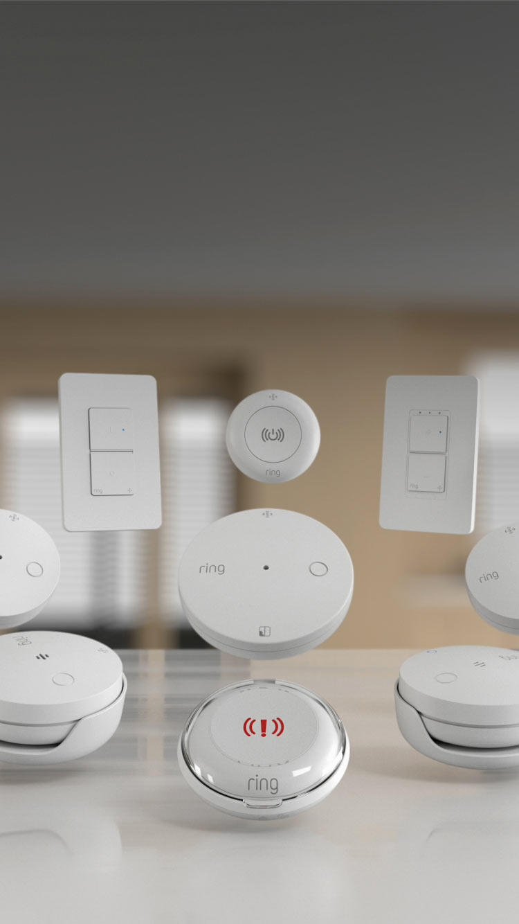 A white Ring Spotlight Cam Plus mounted and illuminated on a building next to a shop window.