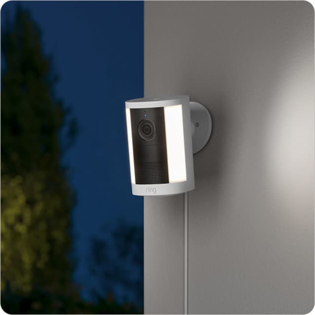 Wall-mounted Spotlight Cam (2nd Gen) on an exterior wall, trees blurred in the dark background.