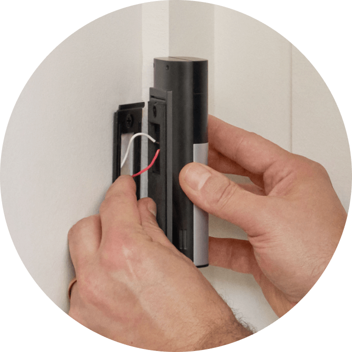 Close-up of hands connecting the home's doorbell wiring to the back of Wired Doorbell Plus (2nd Gen). Device is placed against a white doorframe surface for mounting.