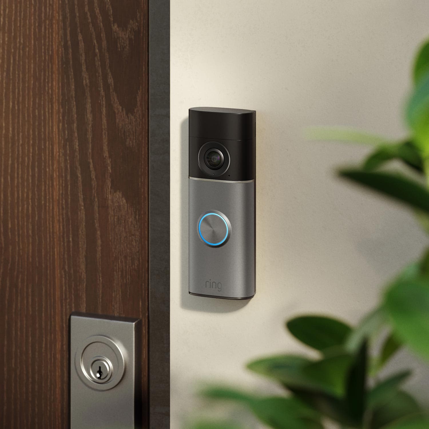 Smart video doorbell with camera mounted on a light wall beside a wooden doorframe in soft daylight.
