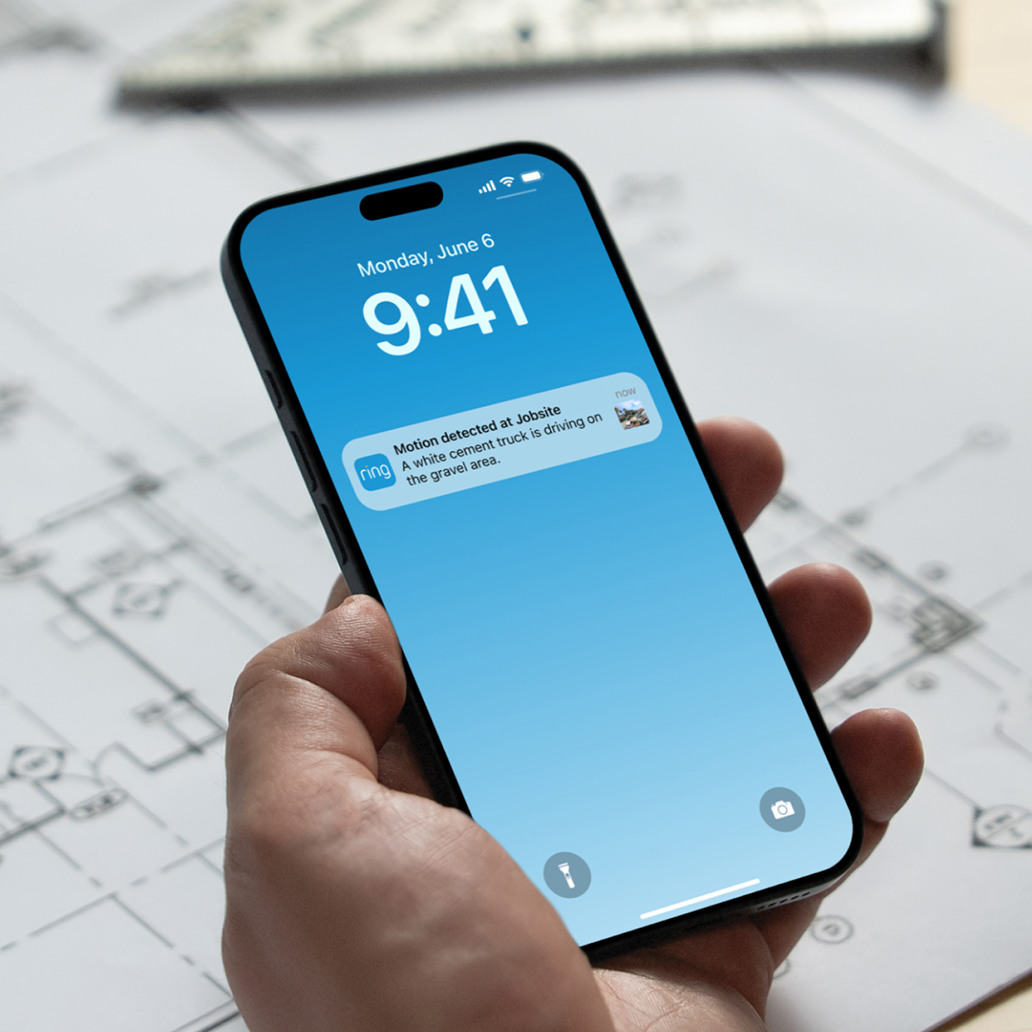 Ring Mobile Security Tower - Solar Panel Kit + 1x Battery - Hand holding a smartphone showing a Ring alert on a blue lock screen, noting motion at a jobsite with a white cement truck.