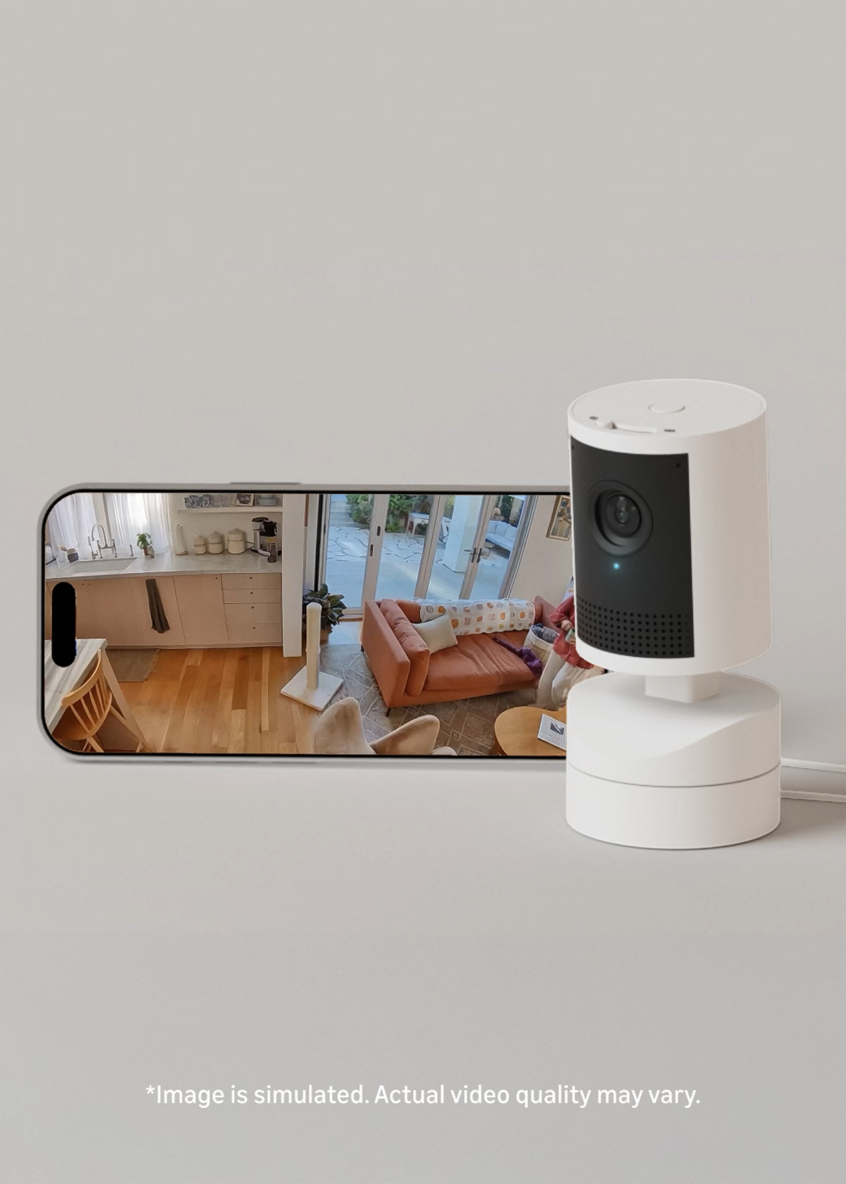 White indoor security camera beside a smartphone showing a live view of a bright living room with sofa, kitchen, and patio doors.