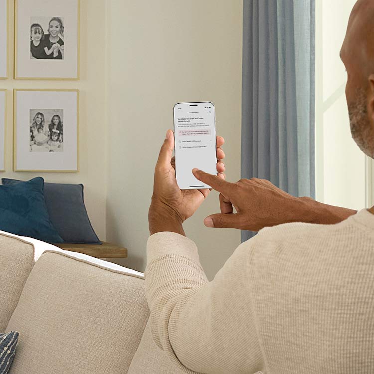 A man holds a mobile phone that shows a low carbon monoxide notification from the Ring app.