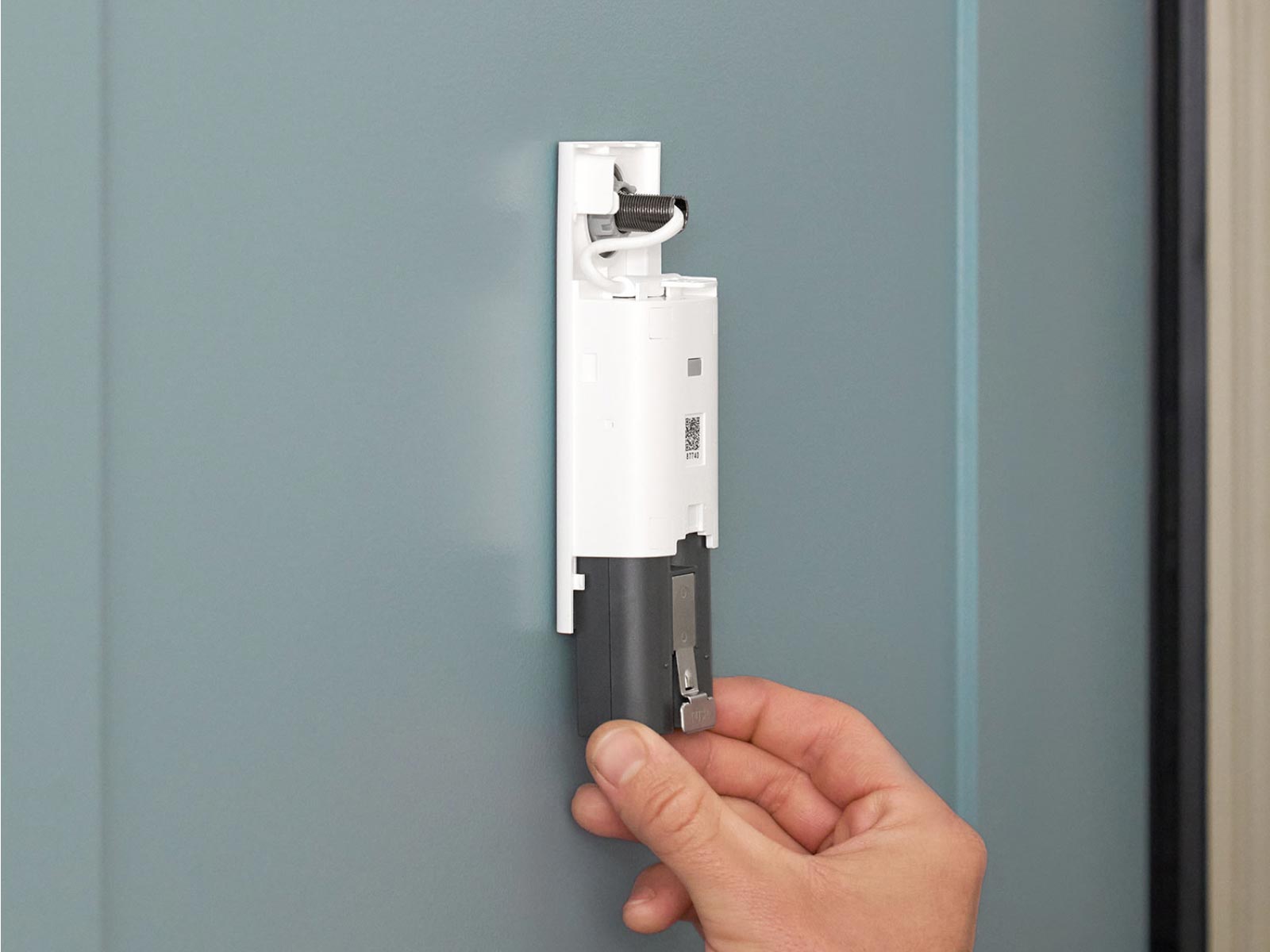 Hand installing a battery doorbell quick release battery pack on a front door, aligning it onto a wall mount bracket.