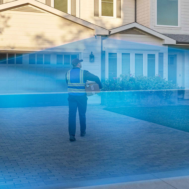 Delivery man walks into a driveway covered in a blue laser graphic extending out from a Ring Outdoor Cam Pro mounted to the house.