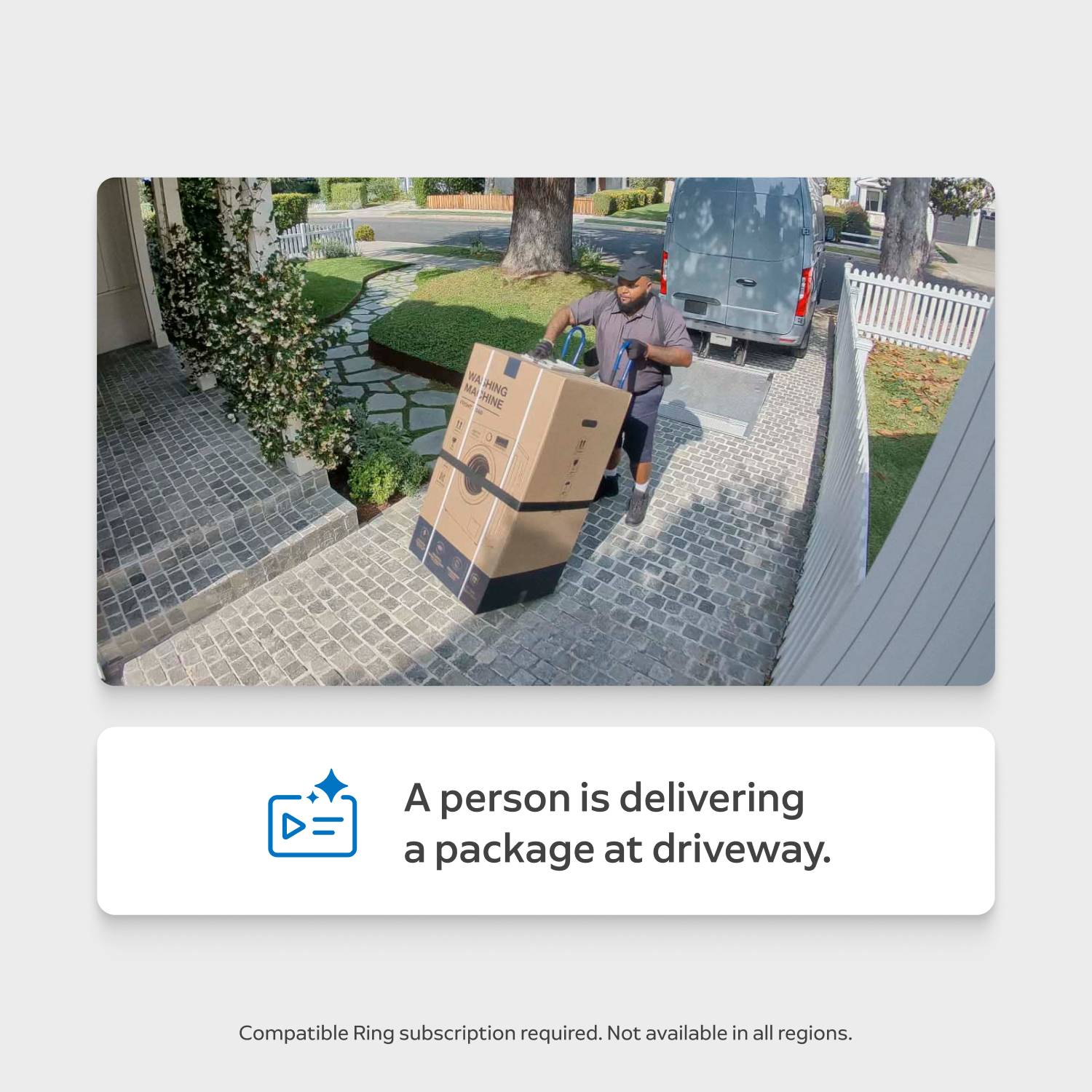 Delivery worker using a hand truck moves a large boxed appliance up a cobblestone driveway toward a house, van parked by white fence.