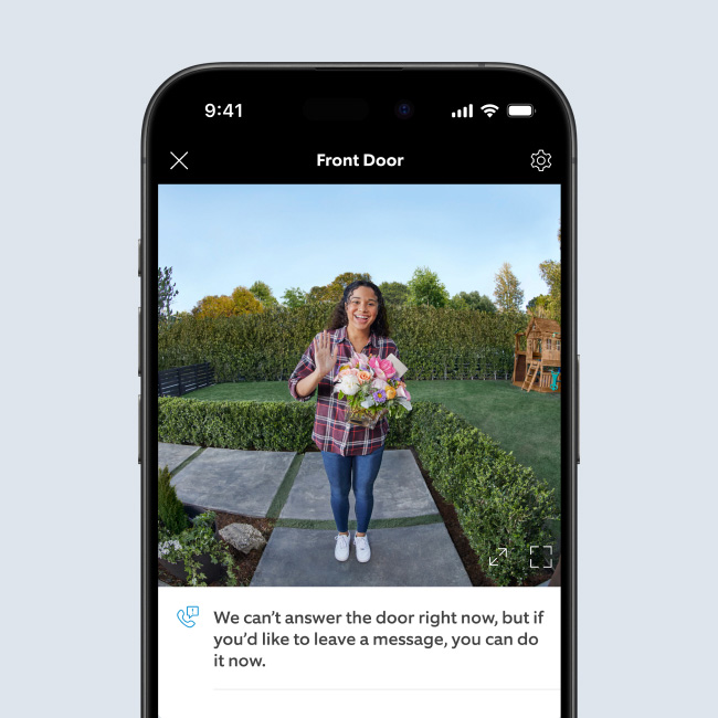 Live Ring Doorbell feed in smartphone of smiling woman holding flowers, with Quick Reply requesting a message be left.