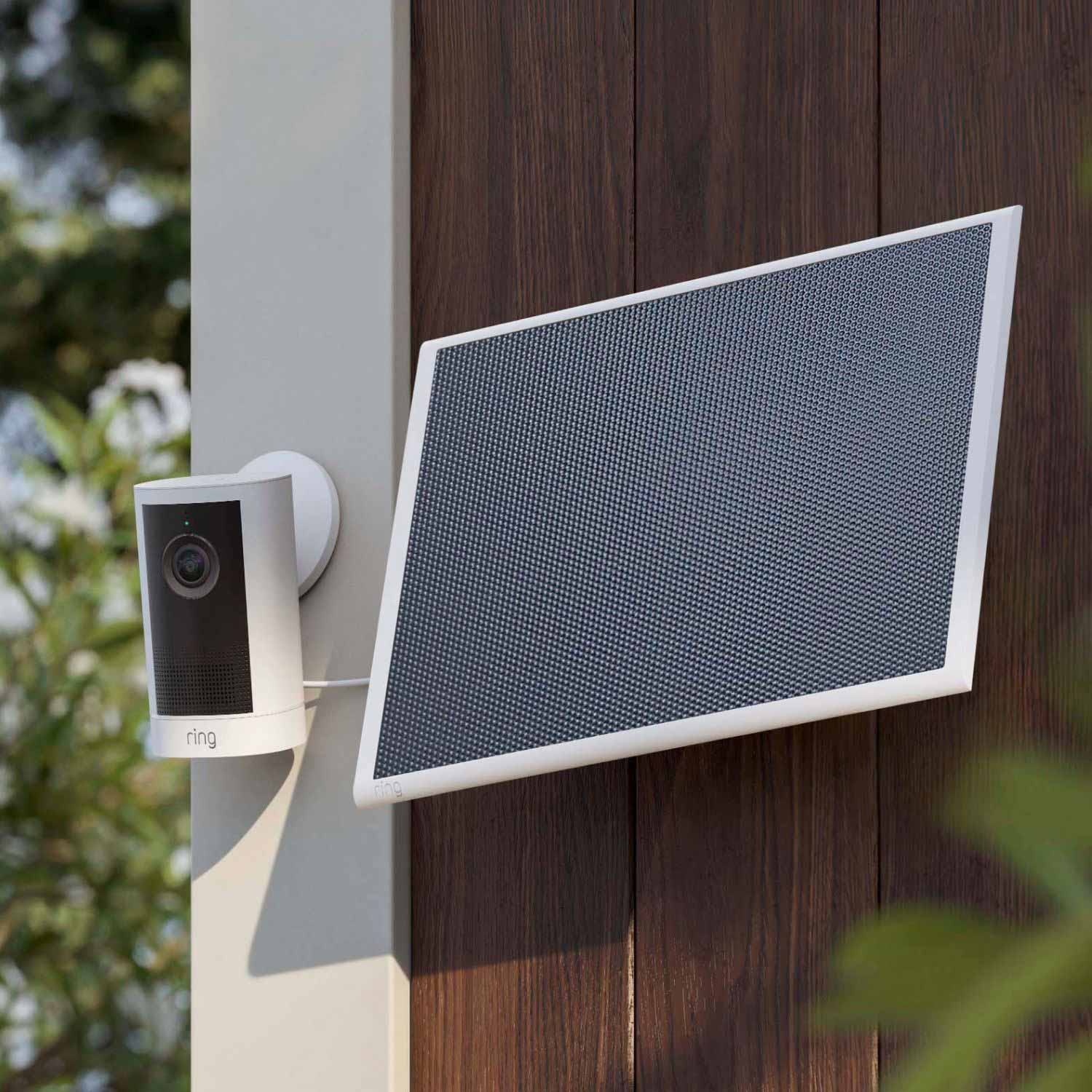 Solar Panel 6W (USB-C) (for Outdoor Cam 4K Plus, Spotlight Cam 4K Plus) - Outdoor Ring camera with a white solar panel mounted on a wooden wall, angled toward a garden with greenery in soft daylight.
