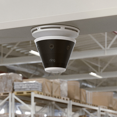Ceiling-mounted Ring dome camera in a warehouse, with shelves of boxed goods and pallets in the background.