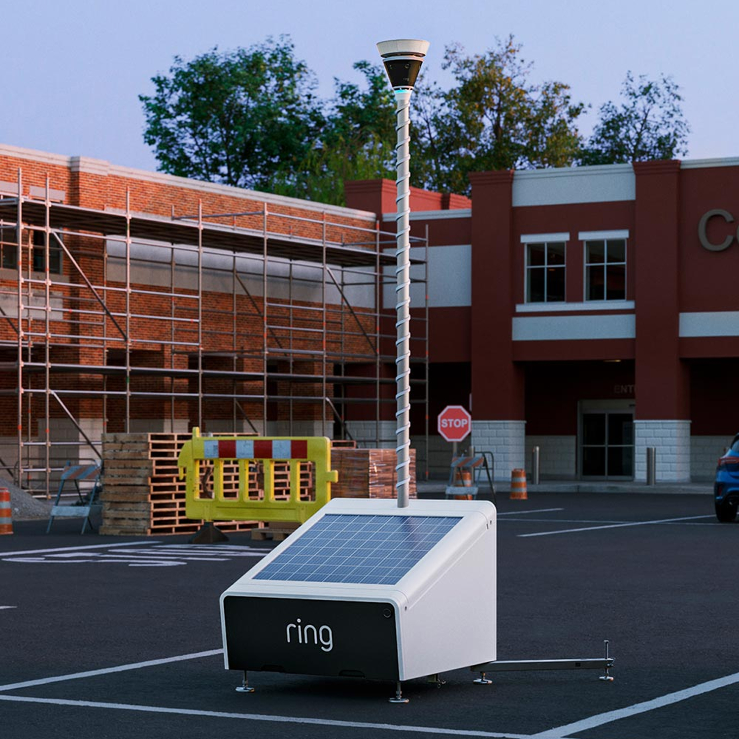 Ring Mobile Security Tower - Solar Panel Kit + 1x Battery - Solar-powered Ring unit with tall pole-mounted camera in a parking lot near a building under construction and traffic barriers.