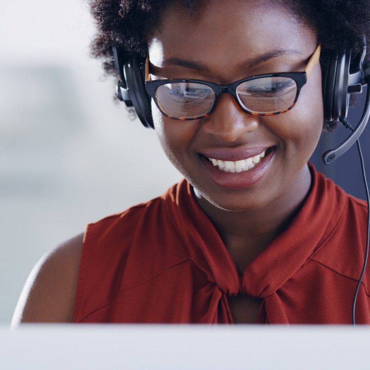 Close-up of a smiling woman wearing a headset and glasses sits at a desk, looking at a laptop screen, representing Ring's security consultation service.