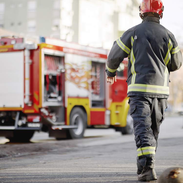 A firefighter in protective gear and a red helmet walks toward a red and yellow fire truck.