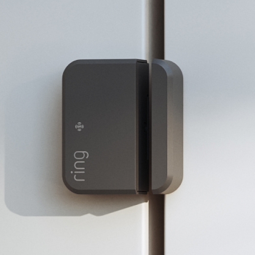 Close-up of a gray Ring contact sensor mounted on a white door frame, showing the two aligned pieces in daylight.