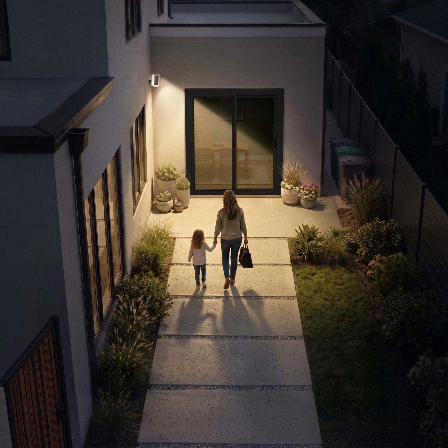 Spotlight Cam 4K Plus - Mother and child walk hand in hand along a lit garden path toward a modern home’s glass patio door at dusk.