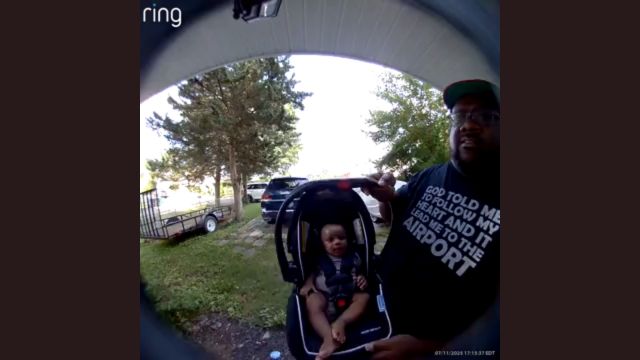 A baby in a car seat is held up to the Ring device and looks right into it.