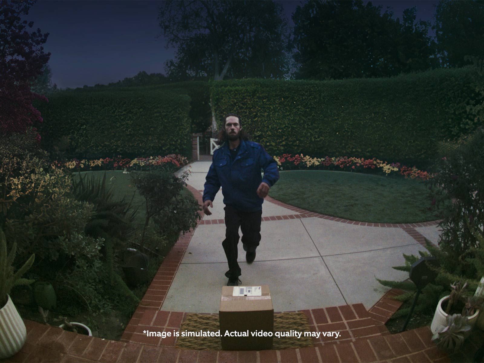 A video taken place at night showing front yard with a visitor walking up to the front door steps. The scene is well-lit, showing clarity even at night. 