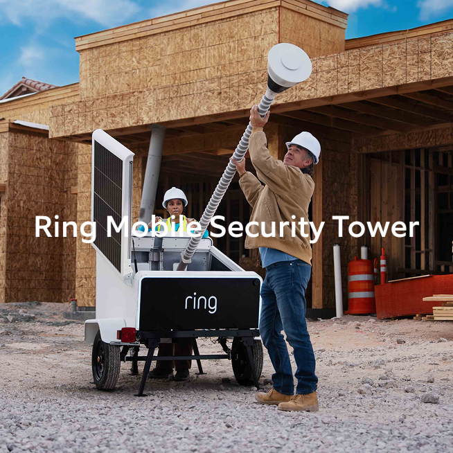 Workers in hard hats raising a Ring Mobile Security Tower beside a blue pickup at a sunny construction site with wood-framed buildings.