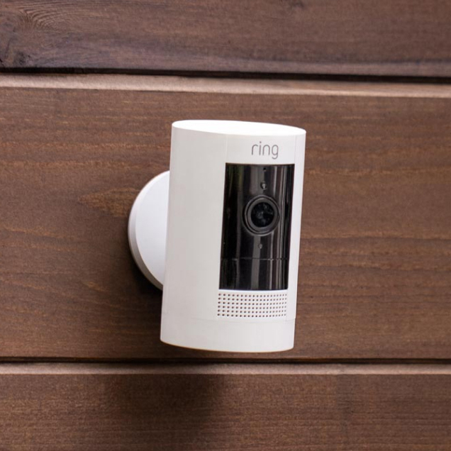 A white Ring Outdoor Cam mounted on wooden siding wall.
