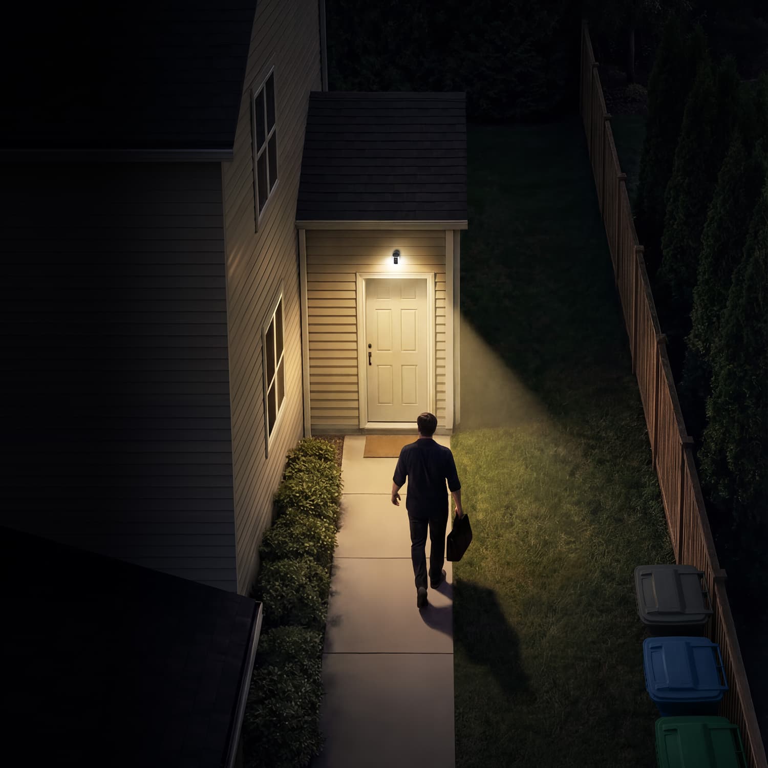 Spotlight Cam (Newest Model) - Person walking up a lit sidewalk toward a back door at night, carrying a bag. Porch light and camera above the door illuminate the entry.